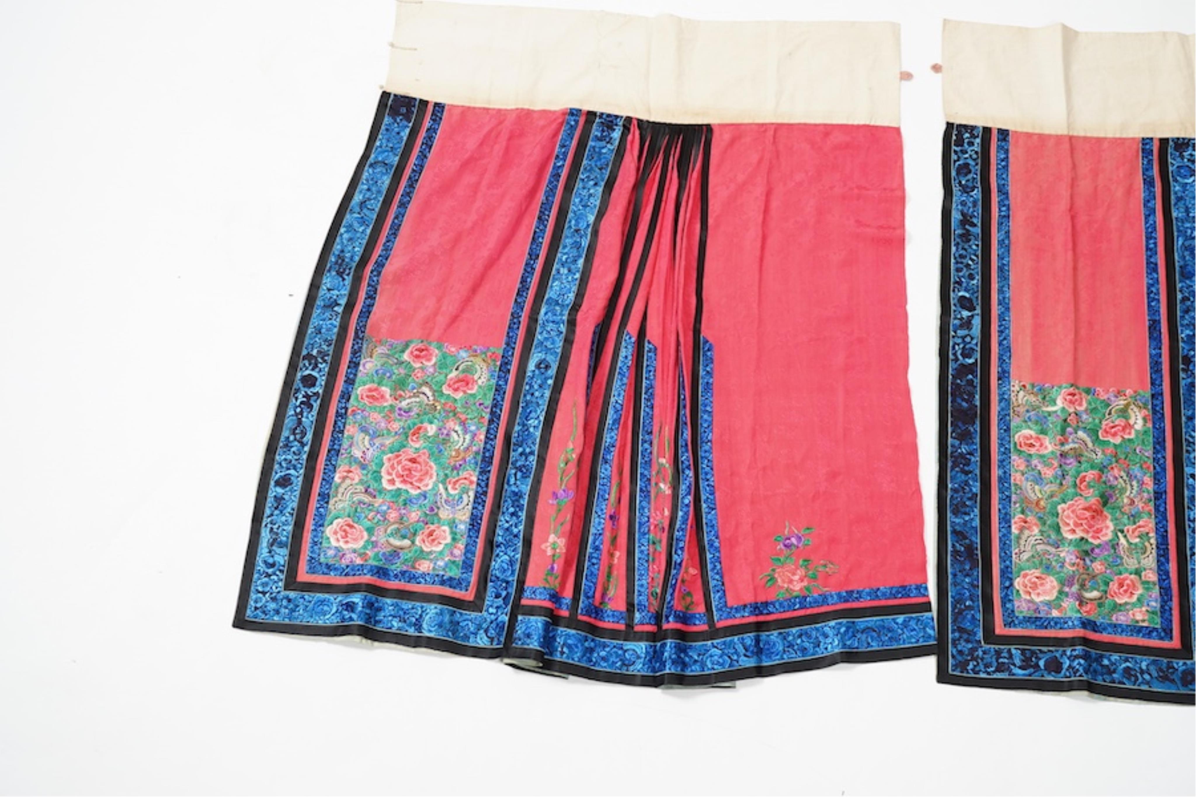 Two late 19th early 20th century Chinese wedding skirts. Made with pink silk damask, embroidered with large decorative silk floral and butterfly front panels bordered by blue embroidered black silk borders between pleats